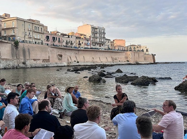  students holding books and listening to a lecture 